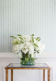 a glass vase with white flowers sitting on top of a table next to a wall