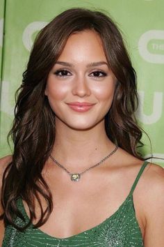 a woman with long hair wearing a green dress and smiling at the camera while standing in front of a green backdrop