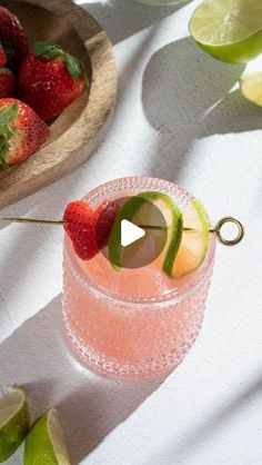 a strawberry margarita garnished with limes and strawberries on a white table