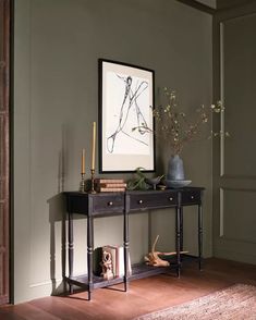 a table with a vase and some candles on it in front of a framed art piece