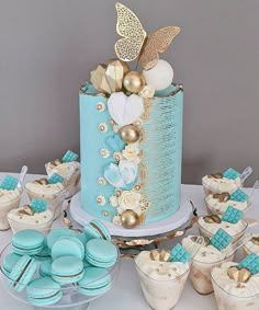 a blue and gold wedding cake surrounded by cupcakes, macaroons and cookies