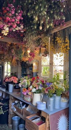 a room filled with lots of potted plants and flowers hanging from the ceiling above