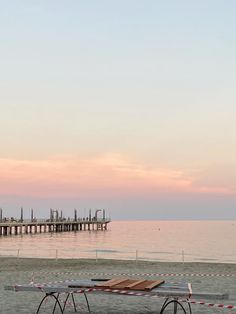 a picnic table sitting on top of a sandy beach next to the ocean with a pier in the background