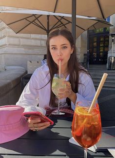 a woman sitting at a table with two drinks in front of her and an umbrella