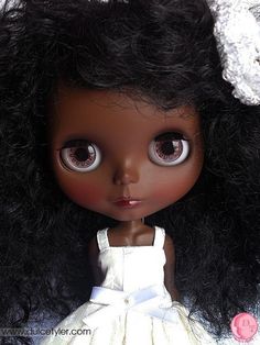 a close up of a doll with big eyes and curly hair wearing a white dress