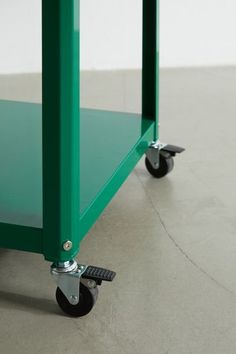 a green cart sitting on top of a cement floor next to a white wall with black wheels