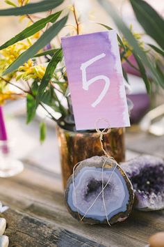 a wooden table topped with a vase filled with purple flowers and a sign that says 5