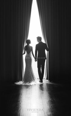 black and white photo of bride and groom holding hands in front of the window at their wedding