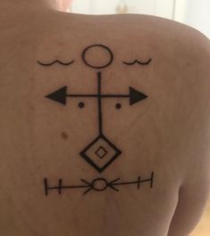 the back of a woman's shoulder with an arrow and cross tattoo on it