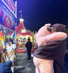 a person hugging a stuffed animal in front of a carnival booth at night time with other people standing around