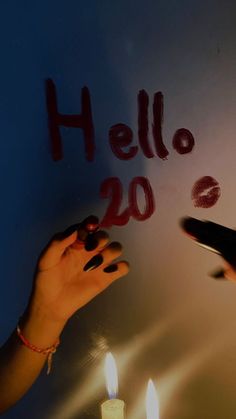 two people writing on a wall with candles in front of them that read hello 20