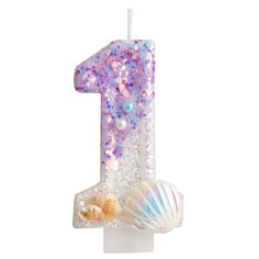 a candle that is shaped like the number one with seashells and pearls on it