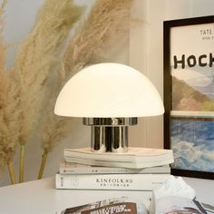 a lamp sitting on top of a white table next to some books and a plant