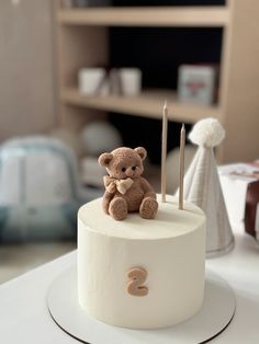 a small teddy bear sitting on top of a white cake with two needles in it