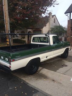 a green and white pick up truck parked on the side of the road in front of a house