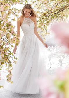 a woman in a white wedding dress standing under a tree with pink flowers on it