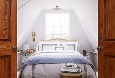 an open door leading to a bed in a room with white walls and wooden floors