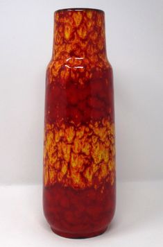 a red and yellow vase sitting on top of a white table