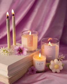 three candles sitting on top of a book next to some flowers and other things that are in front of it