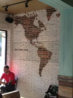 a man sitting at a table in front of a brick wall with a map on it