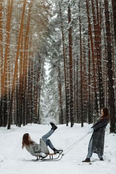 two people in the snow pulling a woman on a sleigh through the woods