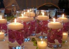 a table topped with lots of glass vases filled with flowers and lit candles on top of it