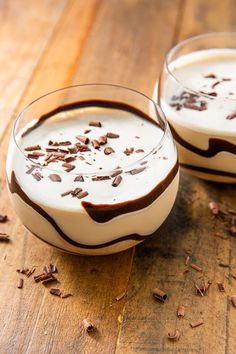 two glasses filled with chocolate and milk on top of a wooden table next to each other