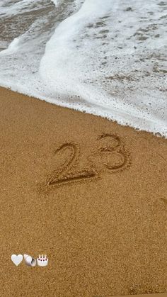 the number twenty two is written in the sand next to an ocean wave and seashells