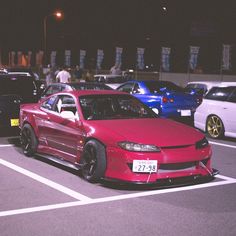 a red car is parked in a parking lot with other cars behind it at night