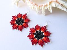 two red and black beaded earrings sitting on top of a white table next to a seashell