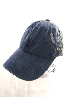 a baseball cap with embroidered flowers on the front and side, sitting on top of a white