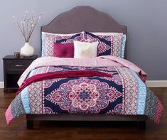 a bed with purple and pink comforters on top of it next to a night stand