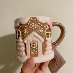 a hand holding a coffee mug with a house on the front and snowflakes on the outside