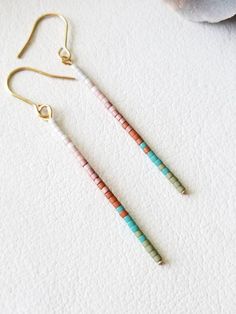 two pairs of earrings with beads hanging from them on top of a white table next to a stuffed animal