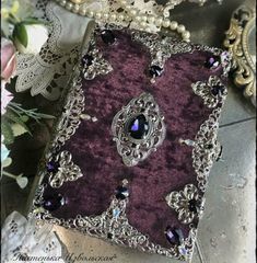 a purple and silver brooch sitting on top of a table next to some flowers