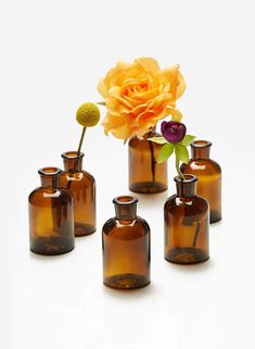 several brown glass vases with flowers in them on a white surface and one has a single yellow rose