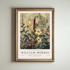 a framed poster hanging on the wall above a vase filled with flowers and plants in front of a white wall