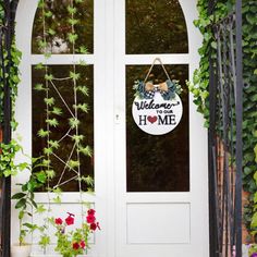 a welcome sign hanging from the side of a white door surrounded by plants and flowers