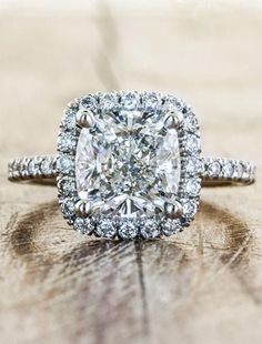 a cushion cut diamond surrounded by round brilliant diamonds on a wooden surface with shallow lighting