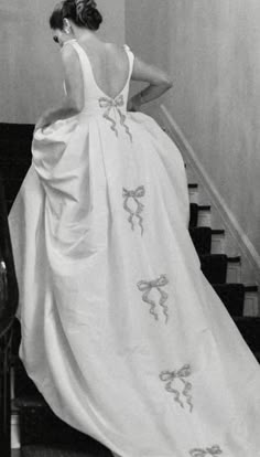 a woman in a white dress is standing at the top of some stairs and looking down