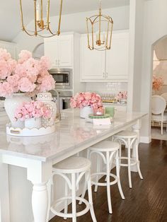 pink flowers are in white vases on the kitchen island