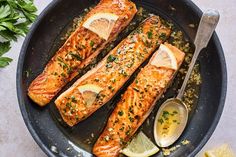 two salmon fillets in a skillet with lemon slices and parsley on the side