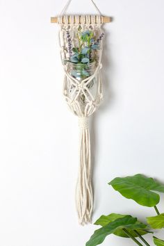 a white macrame hanging from a wall next to a plant with flowers in it