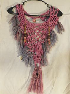 a pink and purple crocheted scarf hanging from a hook on a white sheet