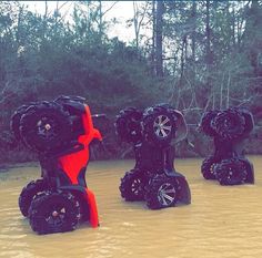 four black and red toy cars are in the water next to some trees with no leaves on them