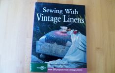 the book sewing with vintage linens is sitting on a wooden table next to a plant