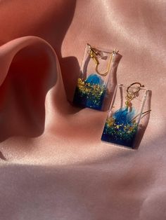 two glass vases with blue and gold designs on them sitting on a pink cloth