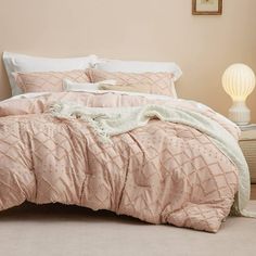 a bed with pink comforter and pillows on top of it next to a lamp