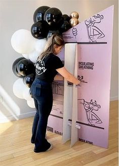 a woman standing in front of a cardboard box with balloons on it and writing on the wall