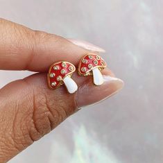 "Add some magic with our adorable dainty Mushroom Stud Earrings! Beautifully detailed with red enamel, sparkling crystals, & plated gold. ♥ Measures approx. ⅜ \" ♥ Materials: dipped in gold plating, glitter flooded resin, & enamel. Posts are titanium - good for sensitive ears! ♥ Packaged in our cute gift box ♥ Designed by & exclusive to Wildflower + Co. ♥ Imported ♥ Product safety - intended for use by adults only; CA residents - see shop policies for Prop 65 warning ♥ Includes 1 pair of earring Red Mushroom Design Earrings Gift, Gold Earrings With Mushroom Design For Gift, Gift Gold Earrings With Mushroom Design, Whimsical Gold Mushroom Earrings, Whimsical Gold Earrings With Mushroom Design, White Mushroom Design Drop Earrings, Cute Dangle Earrings With Mushroom Design, Cute Mushroom Design Dangle Earrings, White Mushroom Design Earrings For Gift